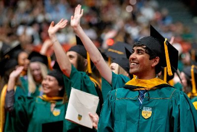 A group of graduates at a commencement ceremony, smiling and waving to the crowd