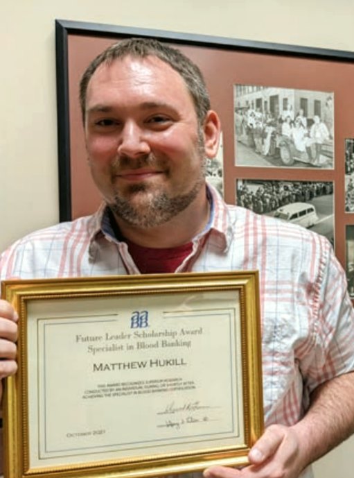 A smiling man holds up a framed award certificate