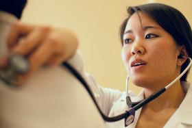 A medical student wearing a white coat uses a stethoscope