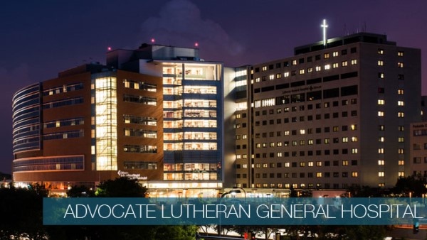 Exterior of Advocate Lutheran General Hospital. It is night and lights are visible through the windows. A large lighted cross sits atop the building.