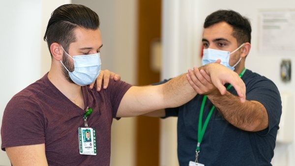 Two PA students wearing masks pratice physical exams