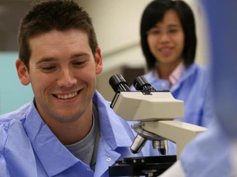 A medical laboratory scientist works diligently at a microscope as a team member looks on.