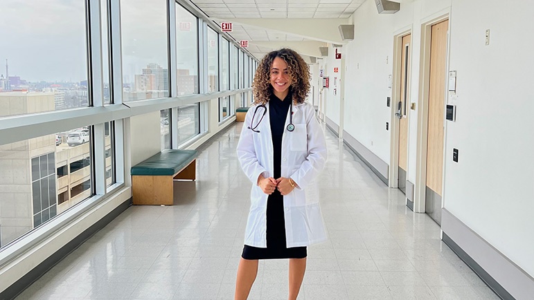 A nurse wearing a white coat stands in a brightly lit corridor