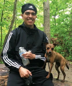 Student Eric Gonzalez outdoors, holding a water bottle and the leash of a small brown dog