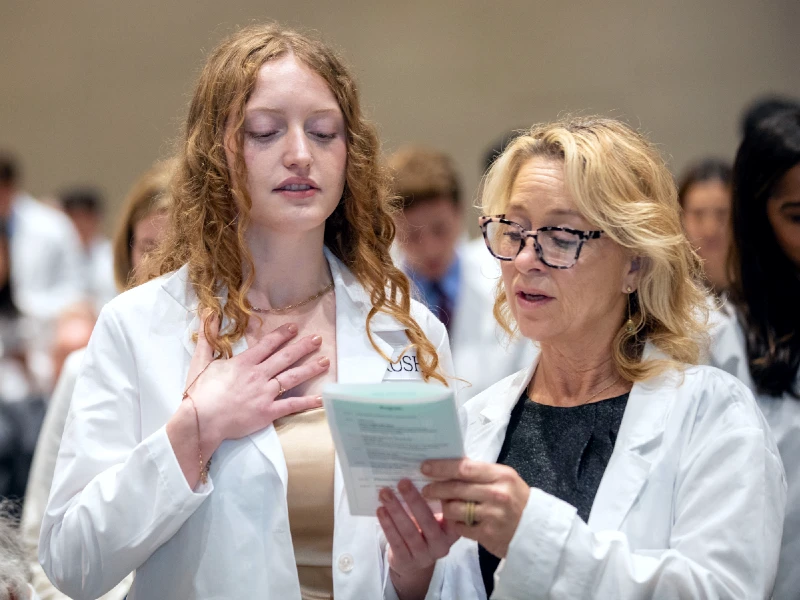 A medical student wearing a white coat holds her hand over her heart
