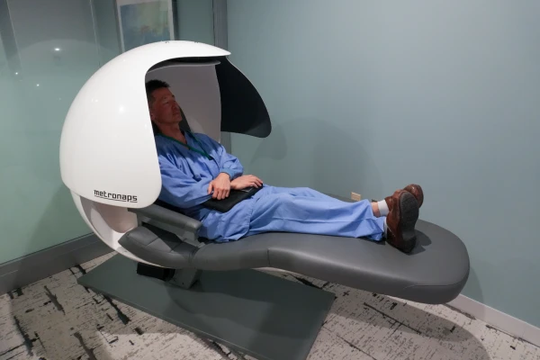 A health care provider wearing blue scrubs reclines in an energy pod