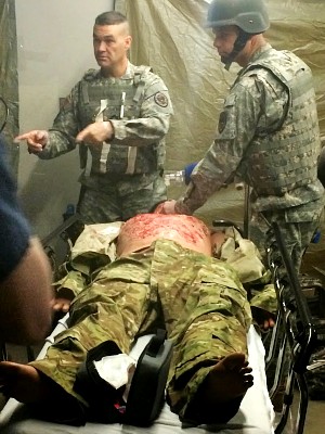 Two trainers in military uniforms demonstrate trauma care on a medical mannequin