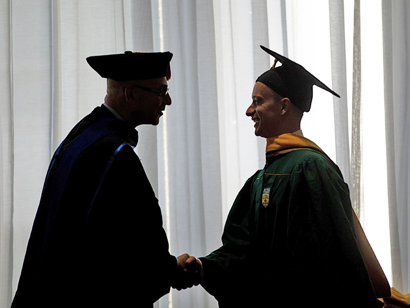 Rush administrator shaking hands with a graduate, seen in silhouette