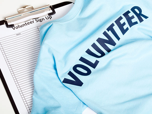 T-shirt printed with the word Volunteer, lying on a clipboard holding a volunteer sign-up sheet
