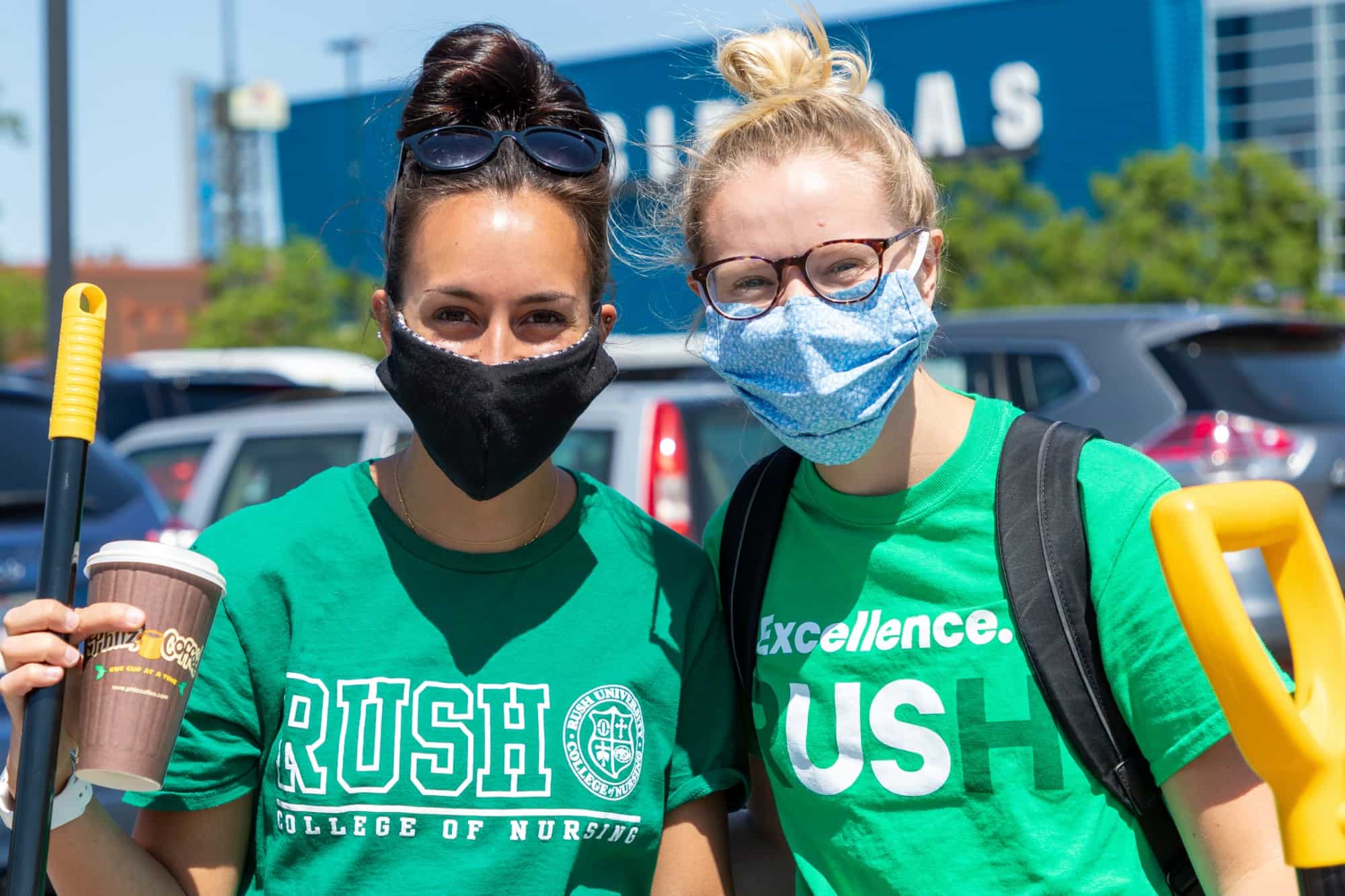 Two students wearing Rush University T-shirts and holding cleaning supplies