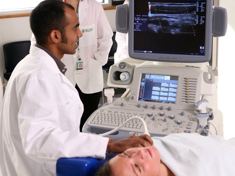 Credentialed vascular sonographer examining patient as vascular ultrasound program student observes
