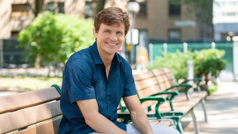 A smiling man seated on a outdoor bench