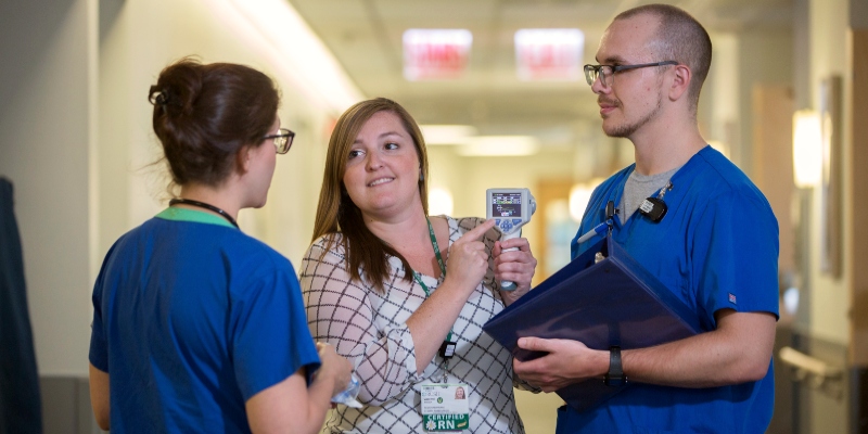 A nurse shows two colleagues a reading on a diagnostic device