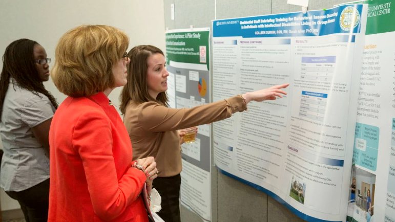 Judges gather around a poster at a research forum