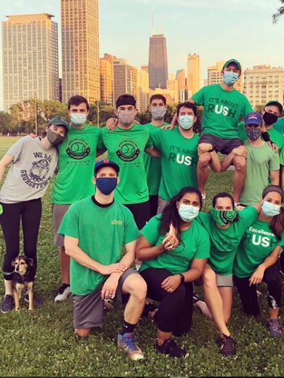 A softball team wearing Rush shirts and face masks pose together in a park