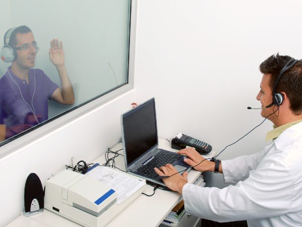 A audiologist conducts a hearing test on a patient in an audiometry booth