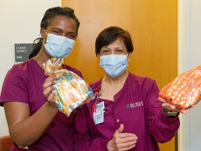 Two health care workers in Rush scrubs and masks hold up colorful care packages