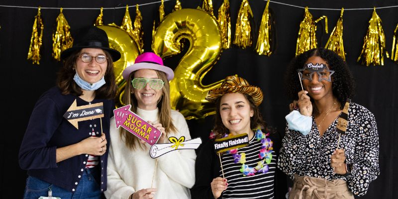 Four students pose with props and accessories in front of a tinsel garland