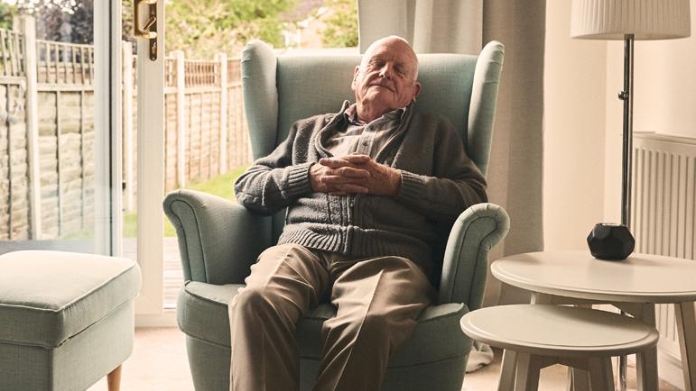 An older adult man sleeps upright in an armchair in a living room