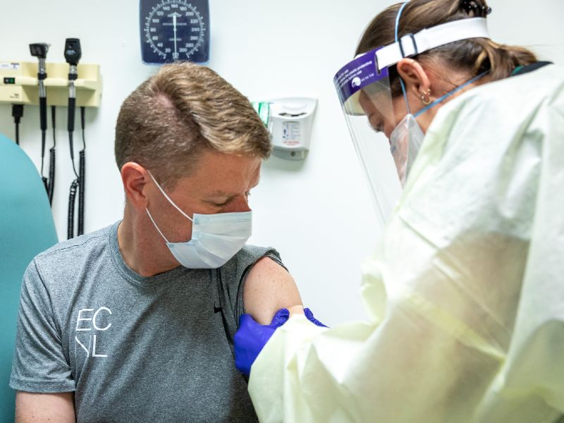 A health care worker wearing protective equipment gives an injection in a patient's shoulder
