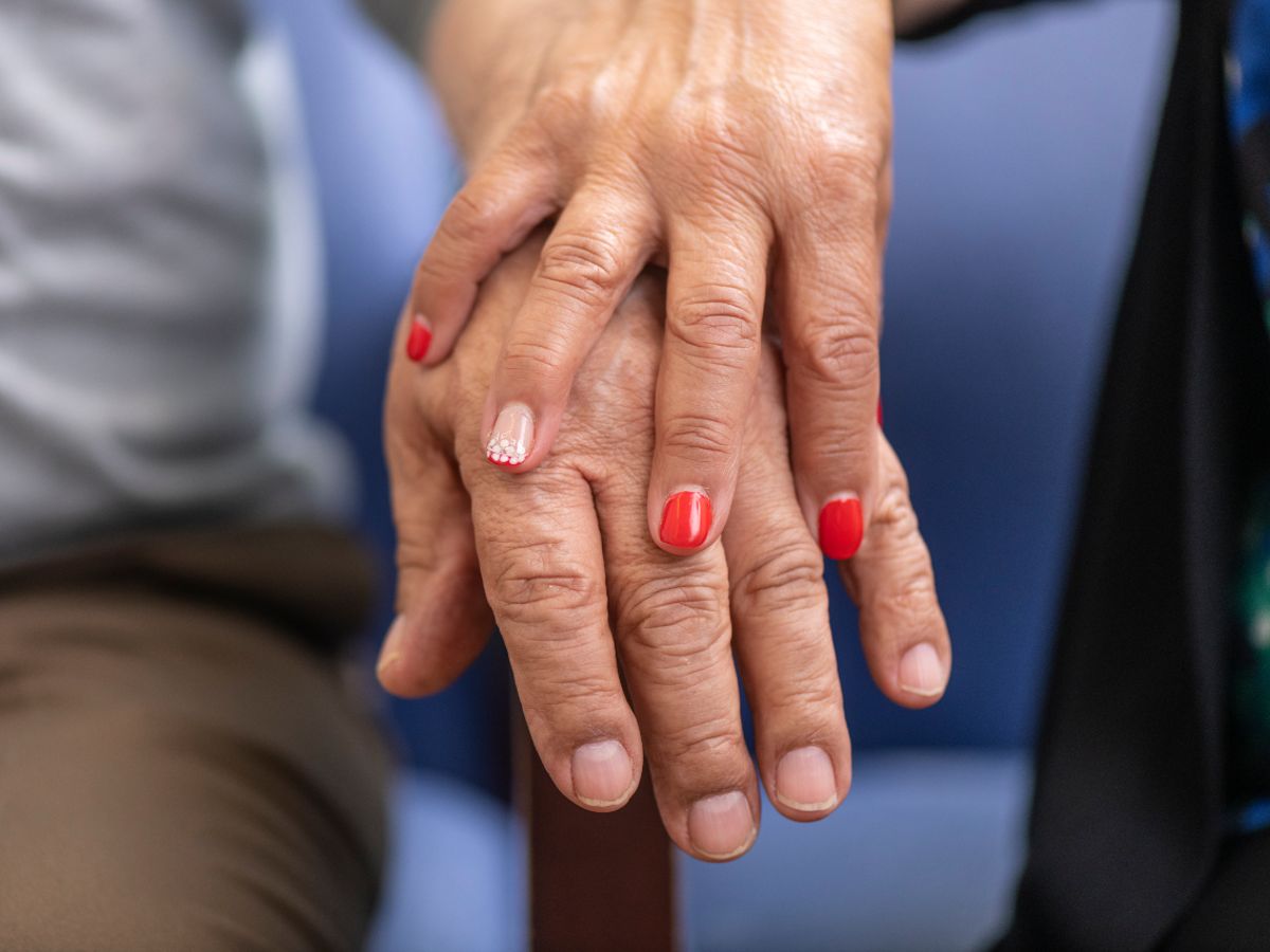 Close-up of the entwined hands of two older adults, one wearing colorful nail polish