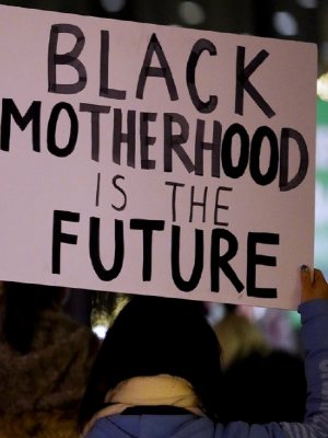 A protester holds up a handmade protest sign that says Black Motherhood is the Future