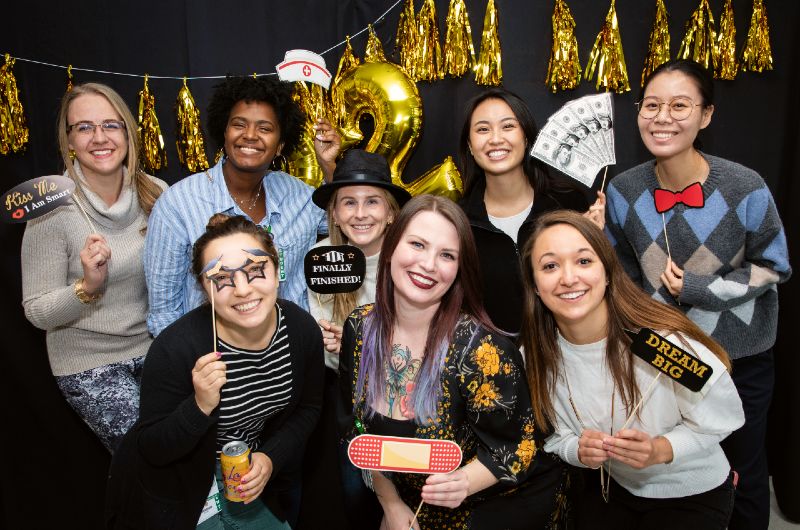 A group of smiling students pose together in front of tinsel garlands with props and hats