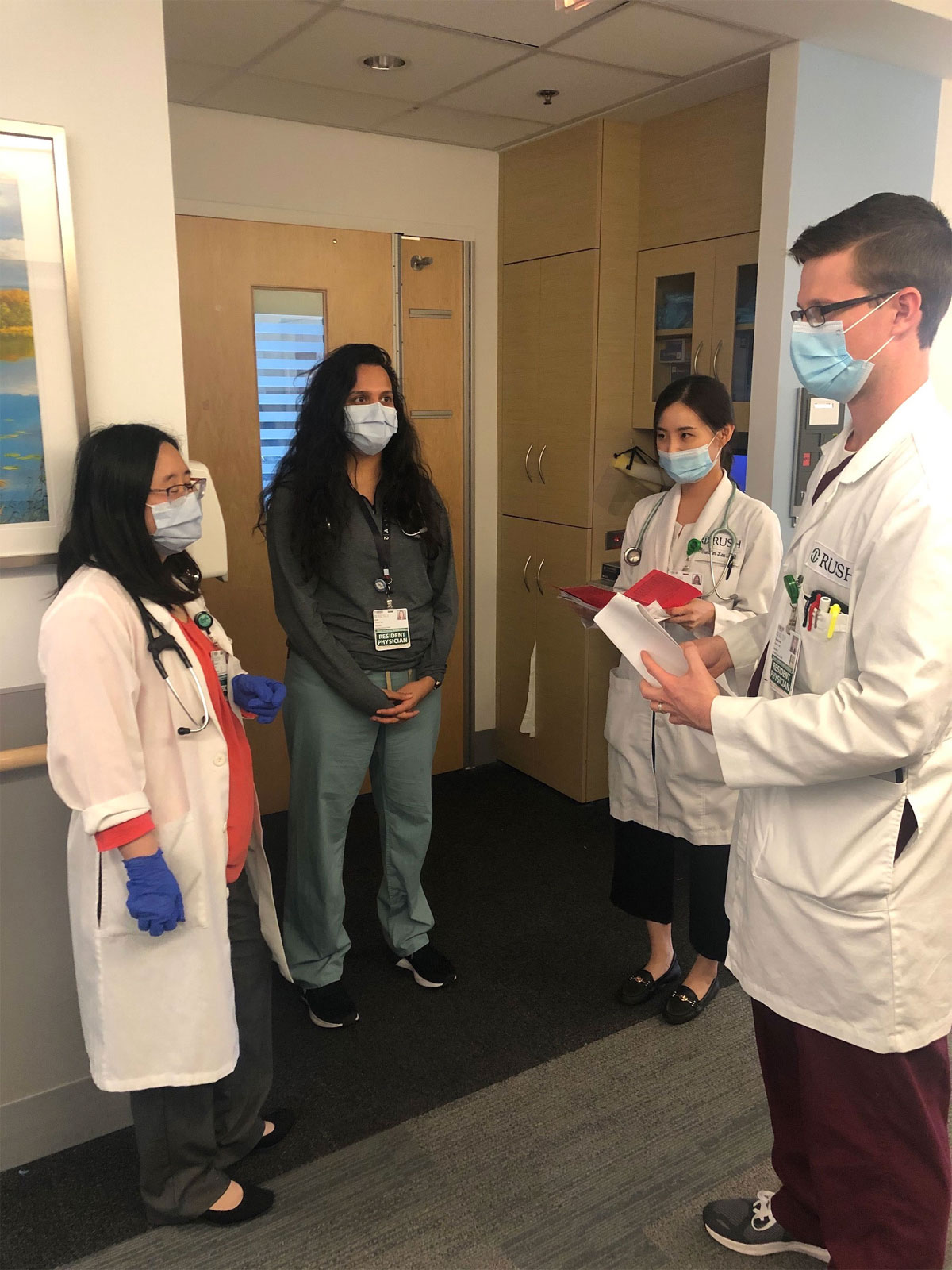 Four fellows wear masks and have a discussion in a hospital hallway.