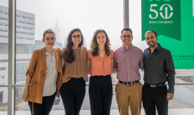 First year fellows gather at RUSH in front of large windows with the Willis Tower in the background and a "50th Anniversary" RUSH sign in the upper right.