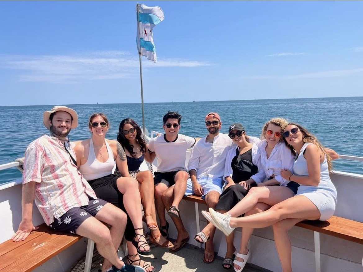 The PGY-3 residents sit on the front of a boat on Lake Michigan with a Chicago flag above them.
