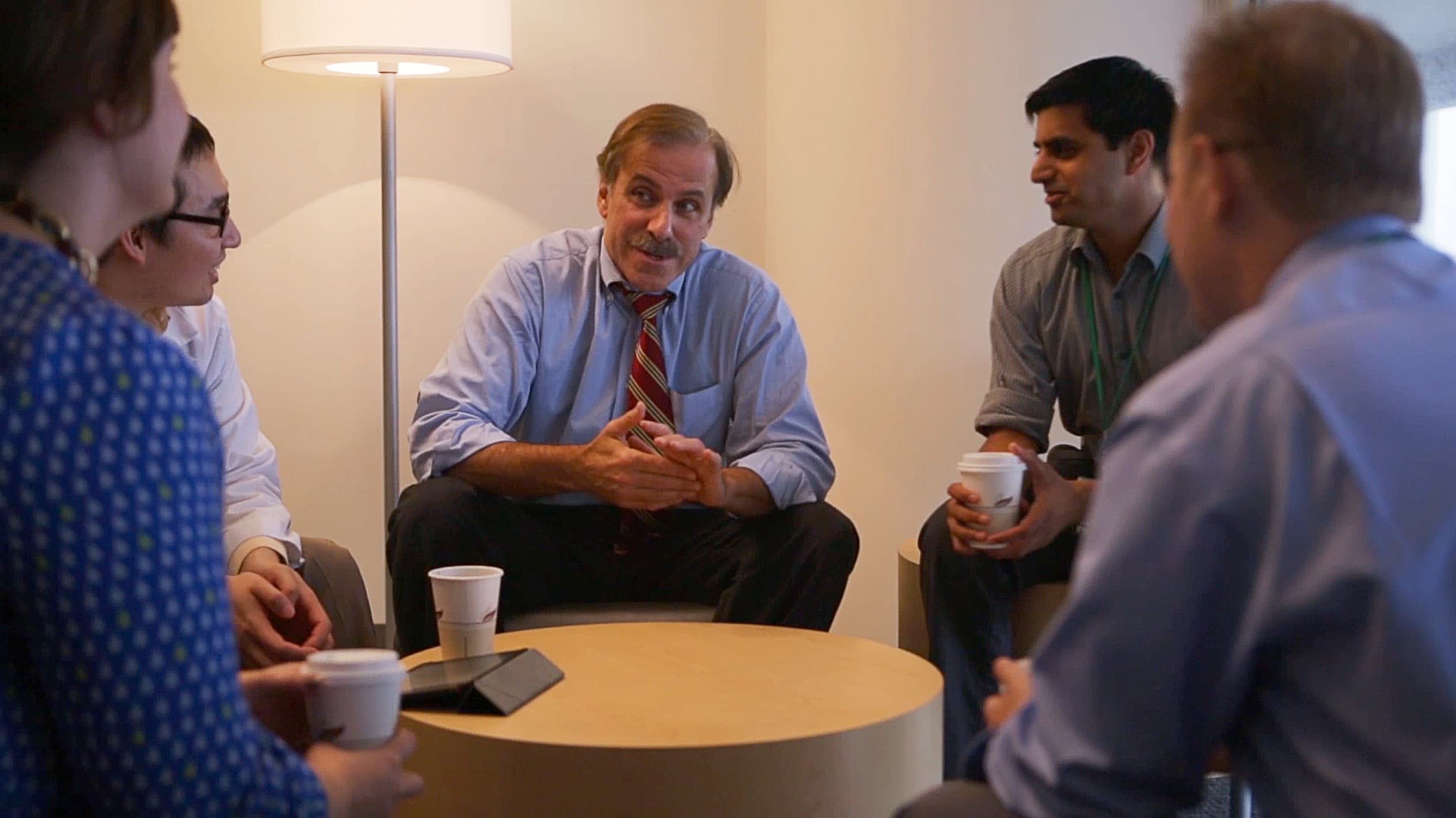 Mark Pollack, MD, has a conversation with residents around a table as they drink coffee.
