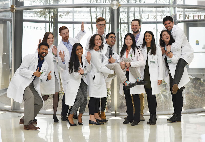 The emergency medicine residents of 2021 make silly poses and faces while dressed in white lab coats in the Atrium of RUSH University Medical Center.