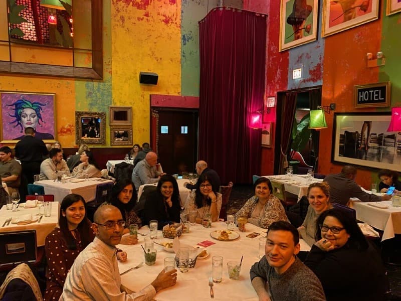 Several fellows sit together at a round table in a crowded restaurant. The walls are multicolored and feature artwork.