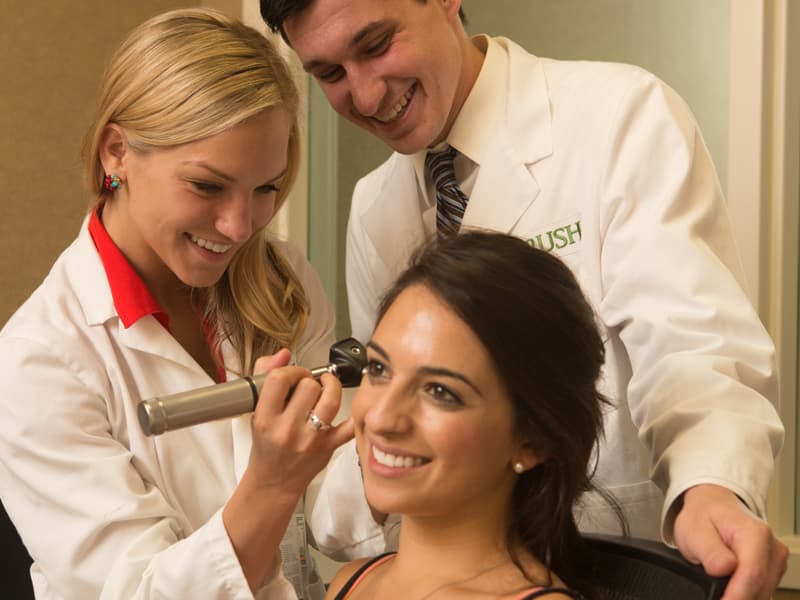 An audiologist examines a patient's ear as a team member looks on.