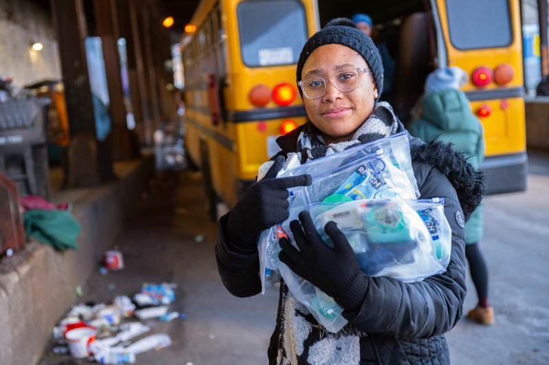 A woman stands under a viaduct holding bags containing personal hygiene products