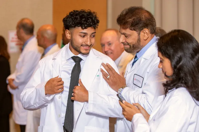 A physician helps an M1 student put on his first white coat