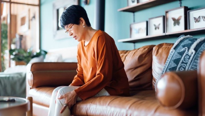 A woman holds her knee and winces in pain.