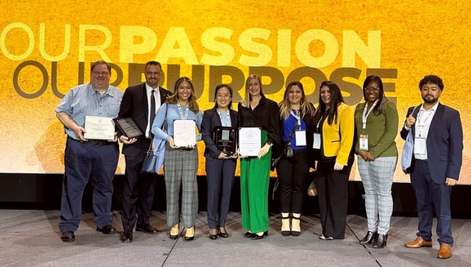 A group of students and faculty pose together on a stage holding award certificates