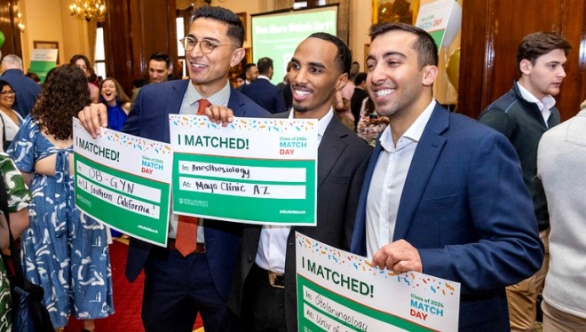 Three students in a crowded room, smiling and holding signs with the words I Matched