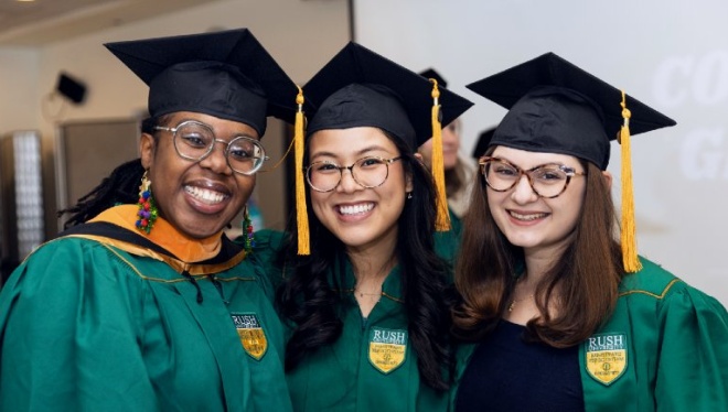 Three people wearing graduation regalia pose and smile for the camera