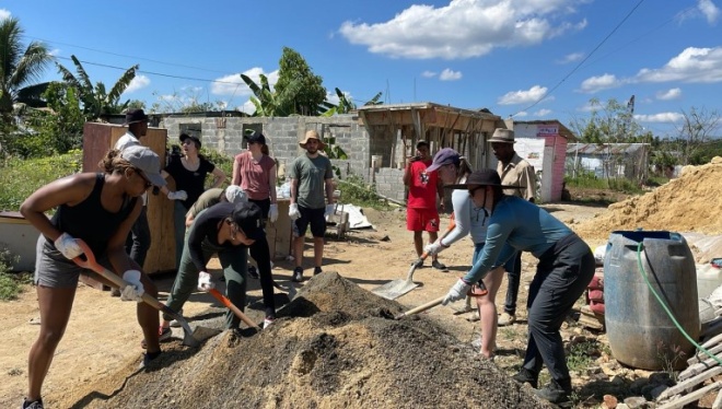 A group of people working outdoors, some holding shovels or digging
