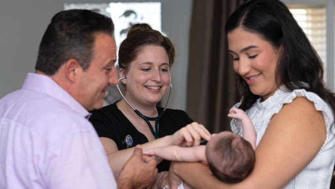 A mother and father hold a baby while a nurse listens to its chest with a stethoscope