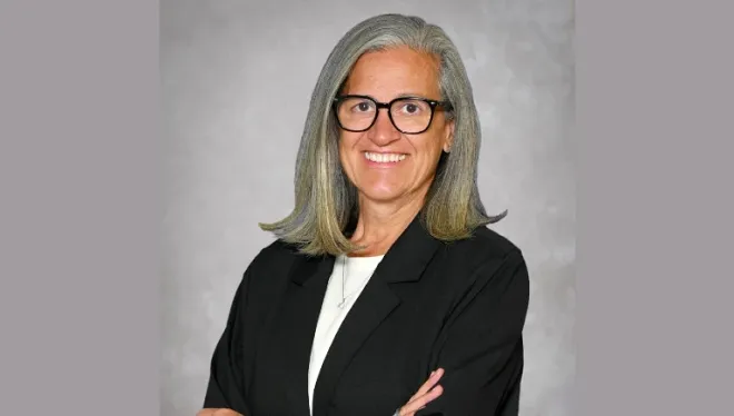 Head shot of Julie Hoff, standing with arms crossed, wearing glasses and a black blazer