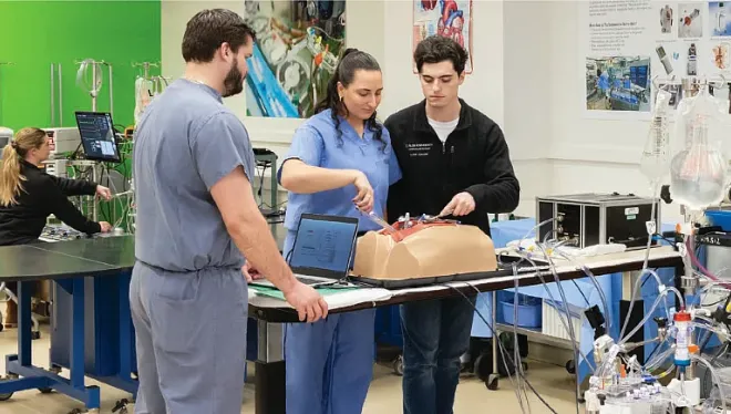Three students demonstrating a procedure on a medical mannikin