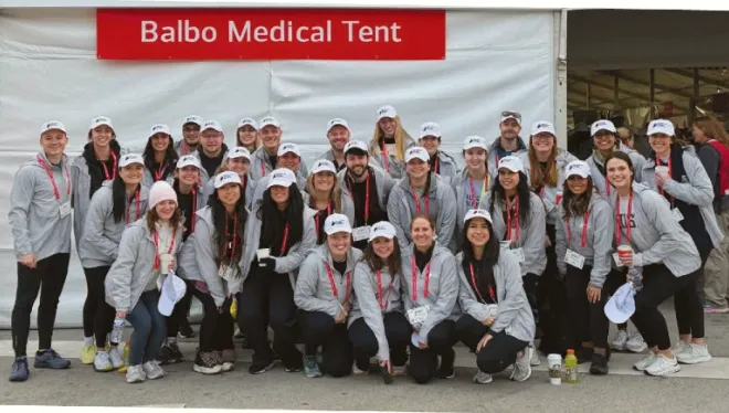 A group of people in matching sweatshirts pose in front of a white event tent with a sign saying Balbo Medical Tent
