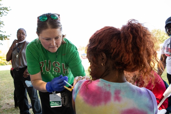 Nurse in green RUSH shirt giving vaccine in left arm of a patient at a community vaccination event. 