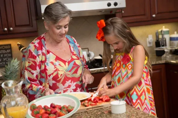 An older woman and a young girl slice strawberries at a kitchen counter