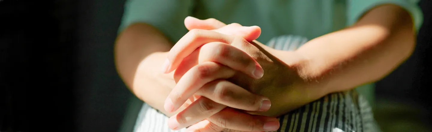 Closeup of a young adult's hands clasped around their knees