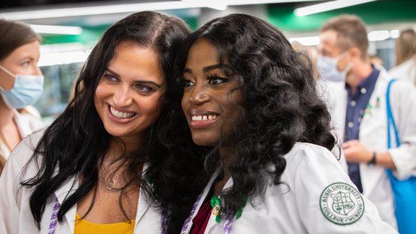 Two nursing students wearing white coats pose for a photo
