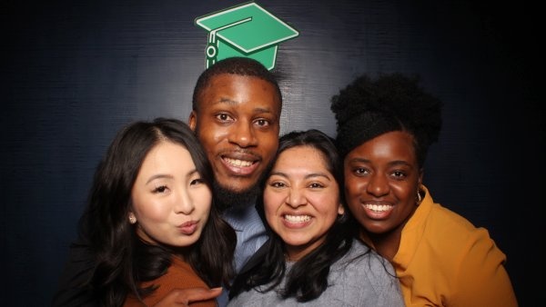 Four people pose together with an illustration of a mortarboard over their heads